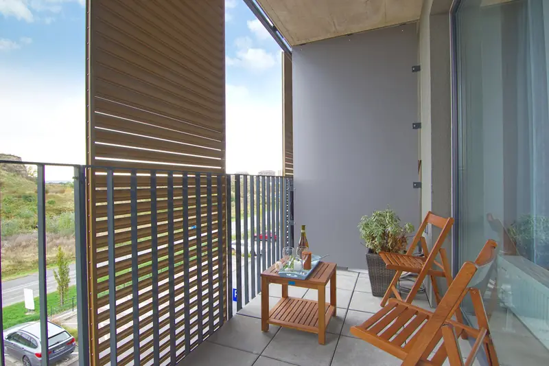 A contemporary balcony featuring wooden chairs, table, and glass wall with a view
