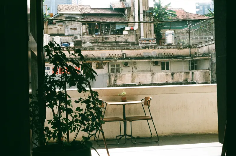A peaceful balcony in an urban setting featuring a table, chairs, and potted plant with rustic views